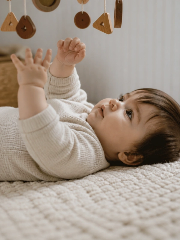 Bebé en actividad de estimulación temprana alcanzando un móvil sensorial — Mimos Desarrollo Integral, Sada, A Coruña